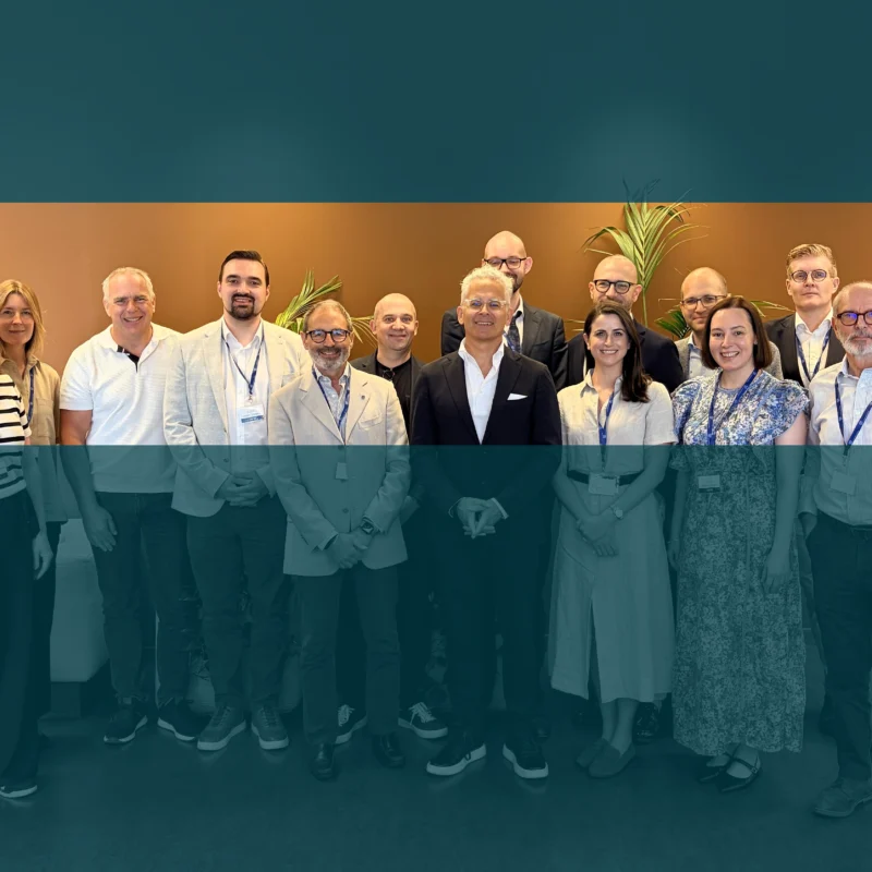 Group of people standing together at an industry event, with a teal overlay and event-style banner design.